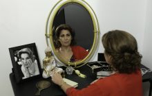 Performer Karin Trachtenberg poses in front of a mirror, a photo of her mother to the side.