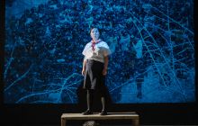 Sora Baek, standing in front of a map, arms stretched out, lit in blue light