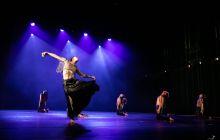 Dancer tries to get away from dancers in white, in dark moody lighting with blue light shining through