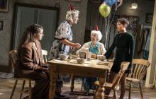 The four actors in the play are pictured round a kitchen table, all looking at each other, balloons in the background.