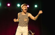 A performer stands in the middle of the frame, surrounded by light in the background.