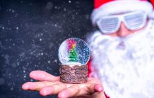 Santa with white glasses holds up a snow globe