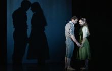 Bruno Micchiardi as John Proctor and Kayla-Maree Tarantolo as Abigail in The Crucible. John is tentatively reaching out to embrace Abigail's hand while their shadows are projected behind them.
