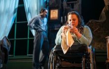 Amy Conachan as Laura sits polishing a glass figure as Christopher Jordan-Marshall as Tom hovers in the background arguing offstage with their mother.