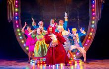 The full cast of Cinderella A Fairytale pose in front of a giast crest, dressed in very bright clothing.