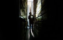 Danny Robins. strides between shelving, covered in box files, moody lighting in black and white