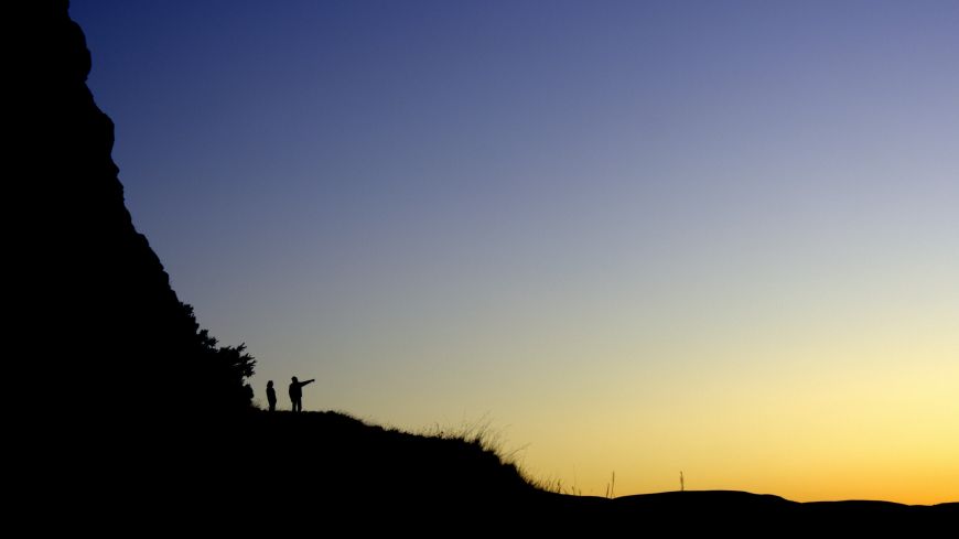 Silhouette of two figures on a hill