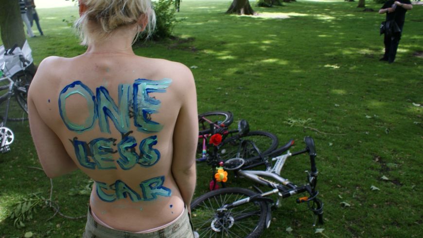 Cyclist at World Naked Bike Ride Edinburgh with "One Less Car" on her back