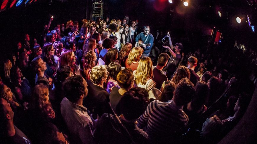 A room full of people singing, black background, with two performers in the middle.