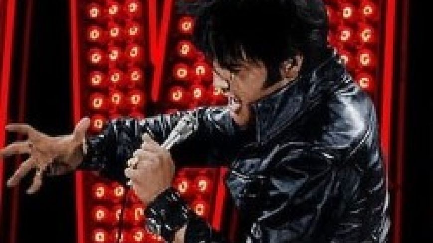 Image of Elvis in black leather outfit with Elvis sign in red lights behind