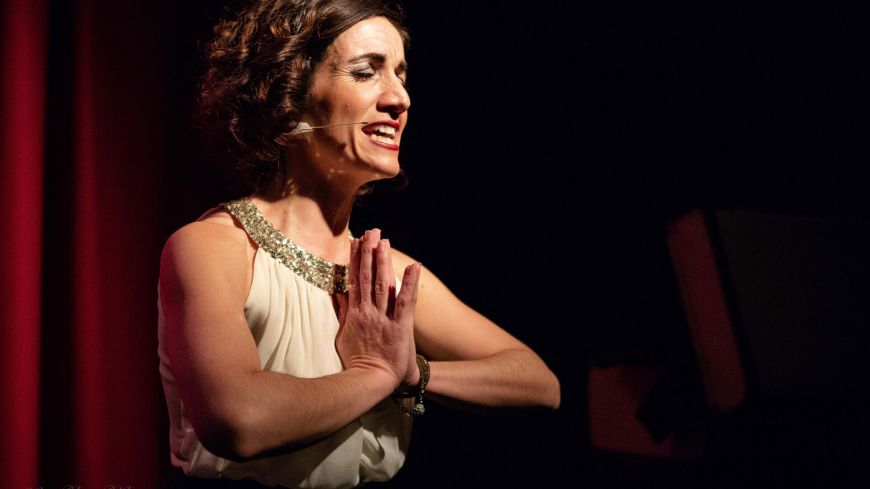 Michaela Burger wearing a white outfit with silver sequins, hands clasped, mid-song