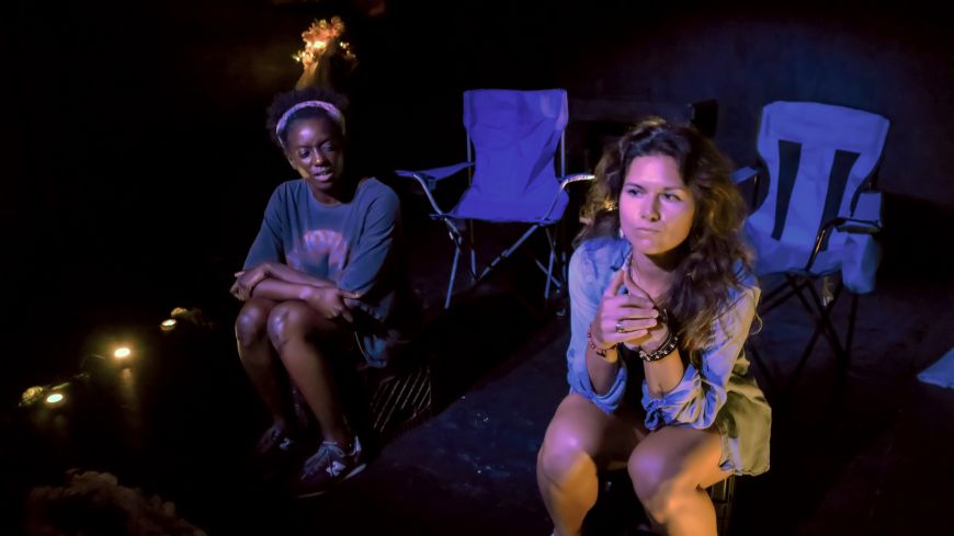 The two actors sit in semi-darkness on folding chairs, looking pensive at the world