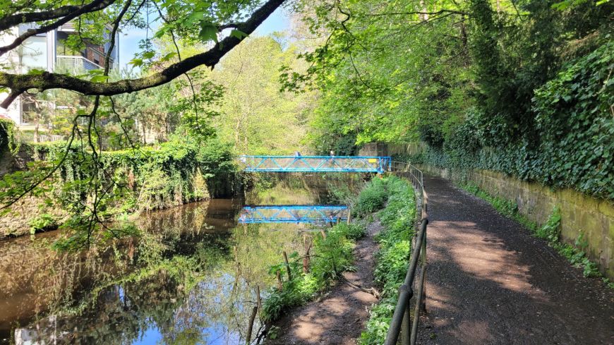 A turquoise footbridge is mirrored on the still waters of the Water of Leith