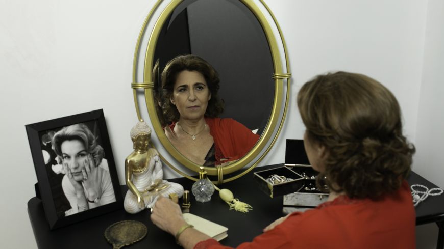 Performer Karin Trachtenberg poses in front of a mirror, a photo of her mother to the side.