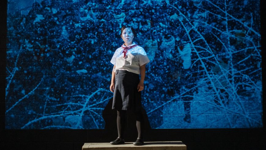 Sora Baek, standing in front of a map, arms stretched out, lit in blue light