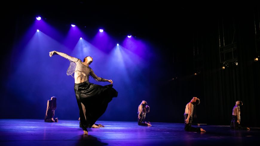 Dancer tries to get away from dancers in white, in dark moody lighting with blue light shining through