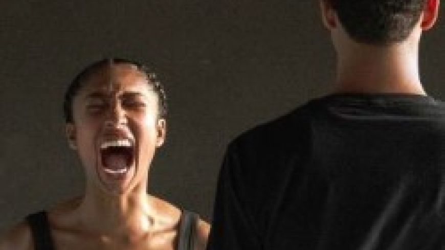 A woman screams with her eyes shut. A man stands with his back to the camera.