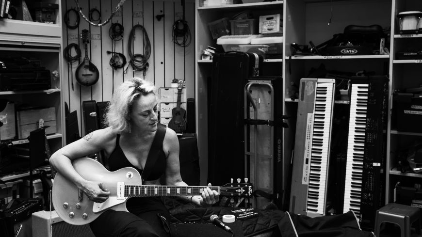 Black and white photo of Biz Lyon playing guitar, in a music room