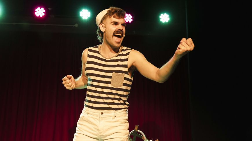 A performer stands in the middle of the frame, surrounded by light in the background.