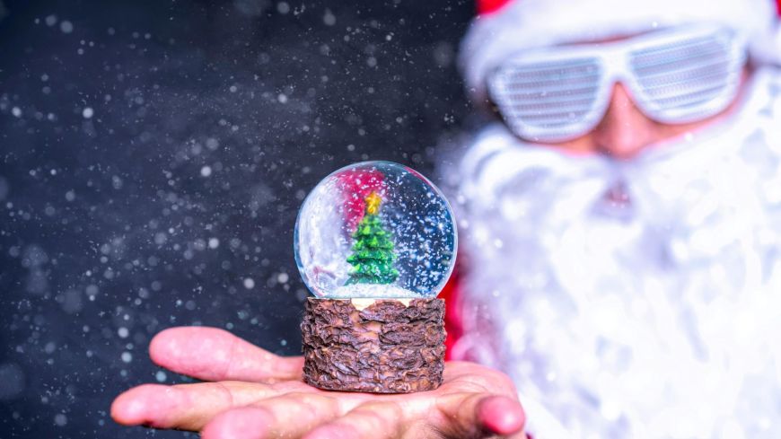 Santa with white glasses holds up a snow globe
