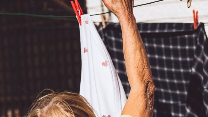 The arm and head of an older woman are shown, hanging out washing on a clothes line.