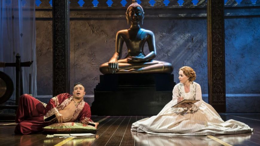 The King and Anna discuss a letter, the King propped up on an elbow and Anna seated on the floor in the King's chambers in front of a large statue of Budda. 