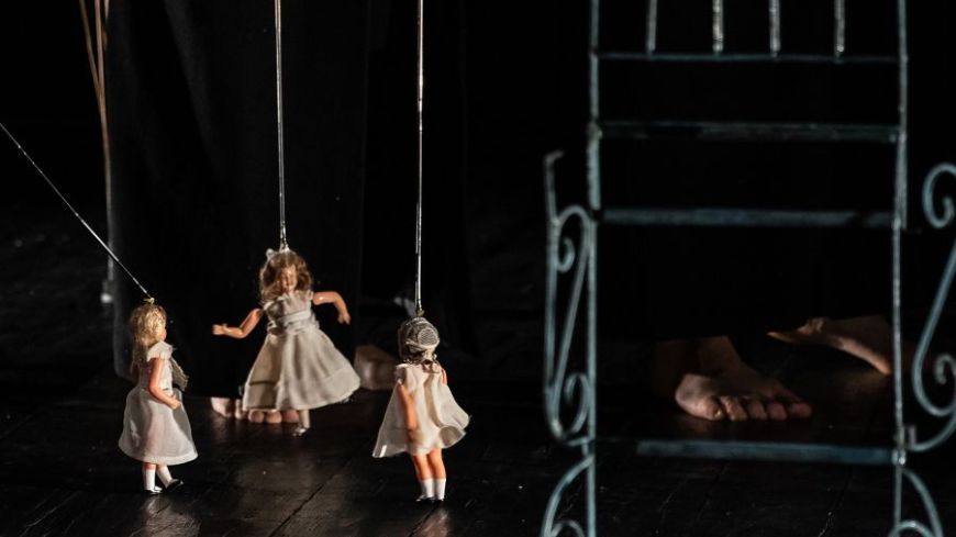 Three dolls dangle from sticks, representing the three women on stage as they explore their lives.