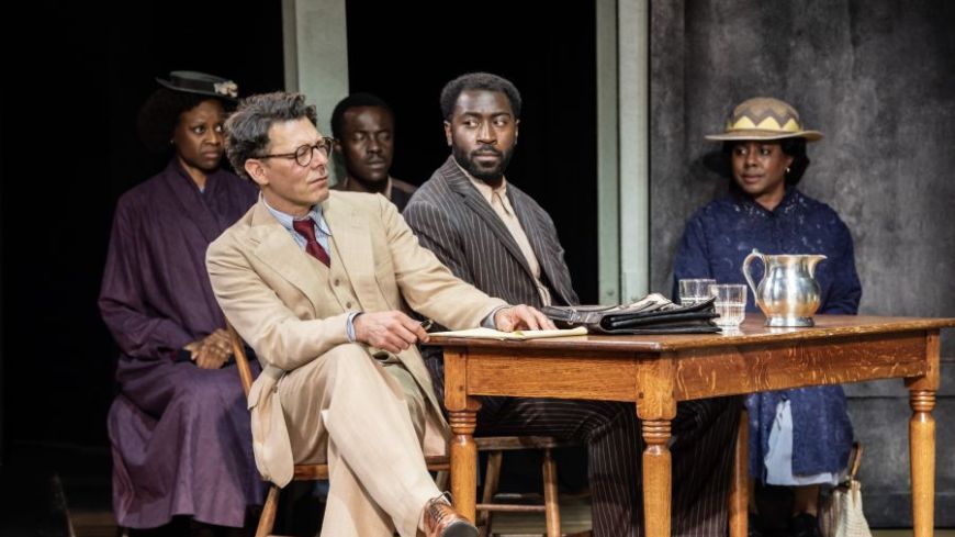Court scene with Richard Coyle as Atticus Finch, Aaron Shosanya as Tom Robinson seated at a table.