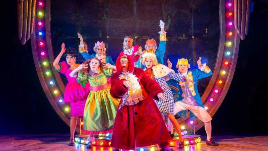 The full cast of Cinderella A Fairytale pose in front of a giast crest, dressed in very bright clothing.