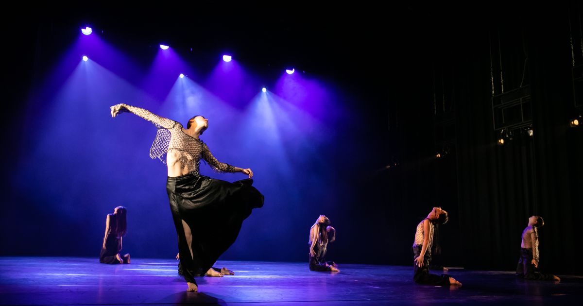 Dancer tries to get away from dancers in white, in dark moody lighting with blue light shining through