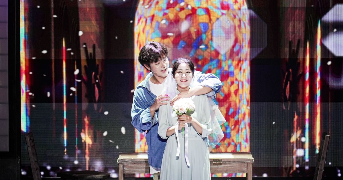 A couple hold each other in the centre of a stage, with a backdrop of light