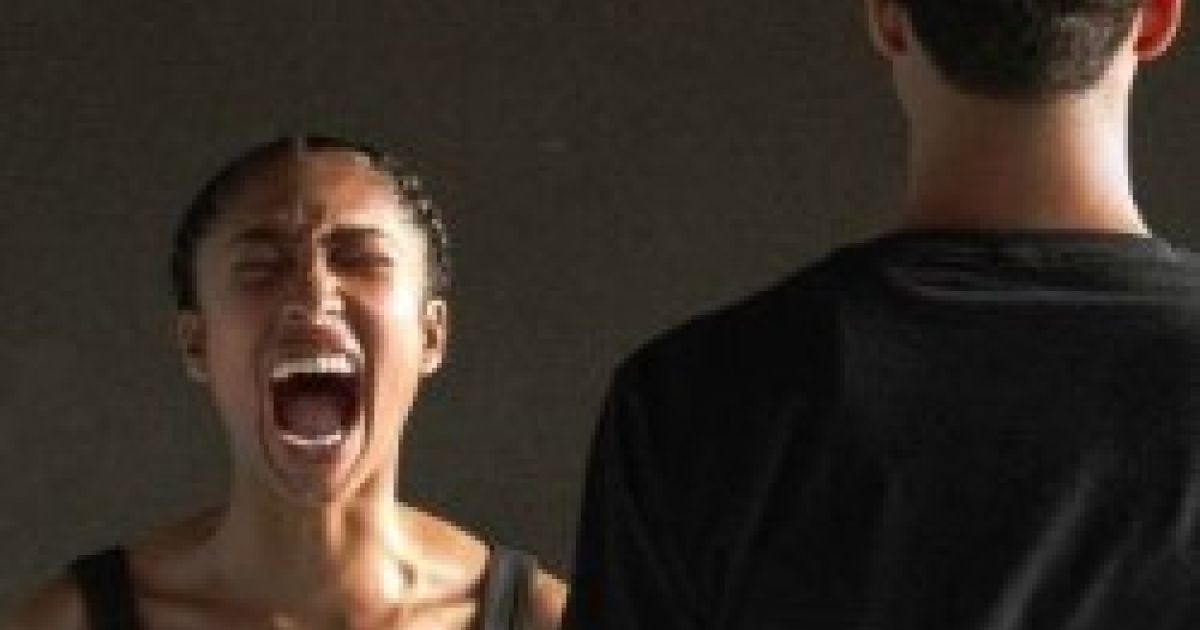 A woman screams with her eyes shut. A man stands with his back to the camera.