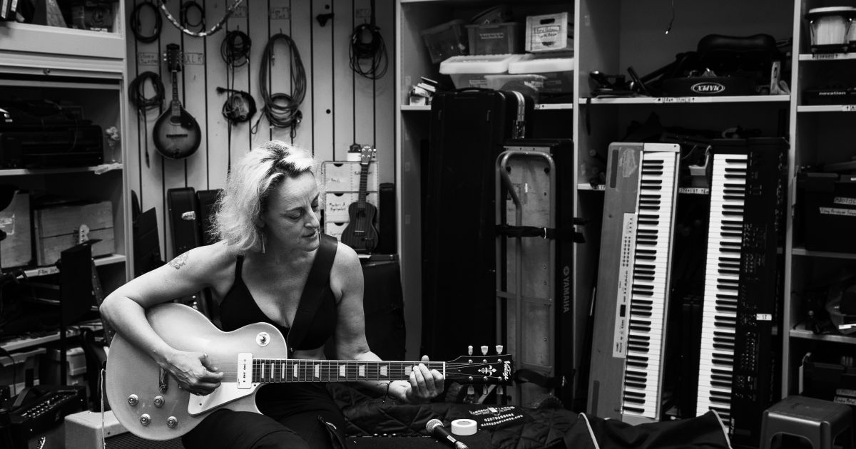 Black and white photo of Biz Lyon playing guitar, in a music room