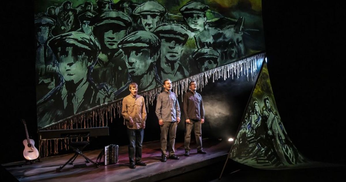 L-R: David Eagle, Sean Cooney and Michael Hughes stand in front of the backdrop of an animation of Hunger Marchers.