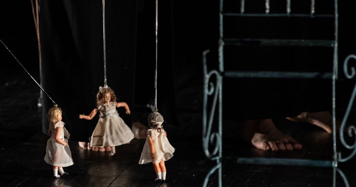 Three dolls dangle from sticks, representing the three women on stage as they explore their lives.
